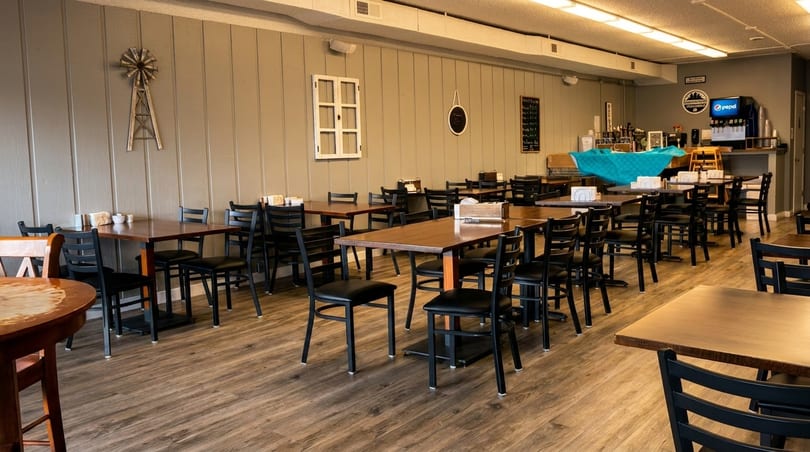 Empty dining room with wooden tables, black chairs, and rustic decor on light gray walls.